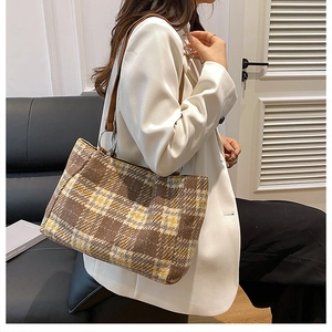 Detailed close-up of a vintage plaid tote bag with brown leather strap on model
