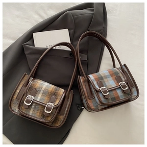 Borse sottobraccio vintage a quadri marroni e blu su sfondo blazer grigio in stile flat lay