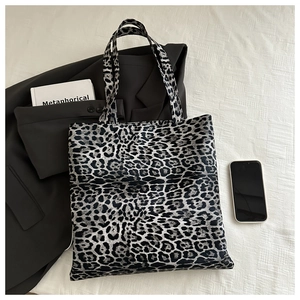 Flat lay of a leopard print canvas tote bag with a black blazer and book for daily commute