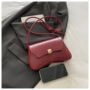 Detail of burgundy crocodile-embossed handbag with golden square buckle and curved base