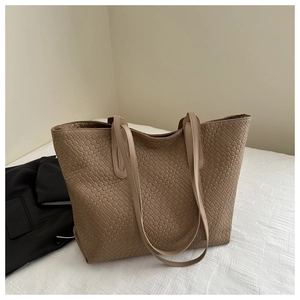 Close-up of brown woven tote bag featuring detailed grid texture on soft white bedding