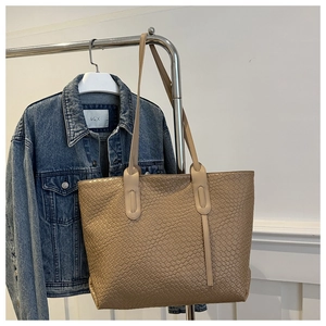 Detailed close-up of a beige woven leather tote bag hanging on a metal hanger