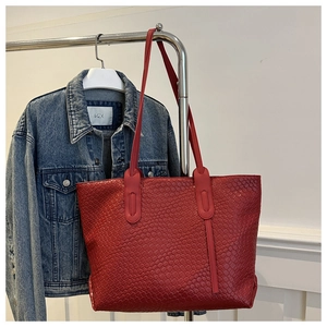 Detail of red woven leather tote bag with large capacity hanging on a metal rack