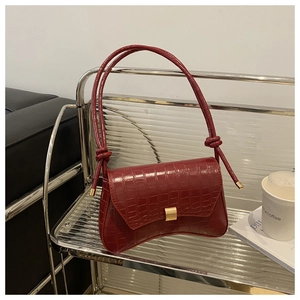Detail of burgundy crocodile-embossed leather with a gold rectangular metal clasp and knot