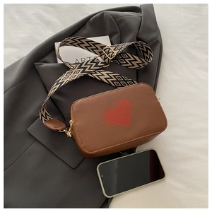 Close-up of brown textured leather bag with red heart and patterned wide shoulder strap