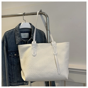 Close-up of white woven leather tote bag texture hanging next to blue denim jacket