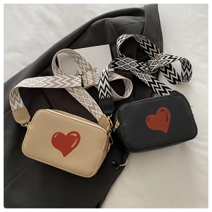 Detail of trendy heart print camera bags in beige and black with woven wide straps