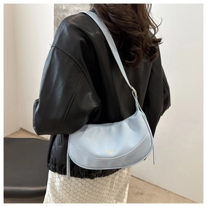 Close-up of light blue crescent bag with litchi grain texture worn by a model