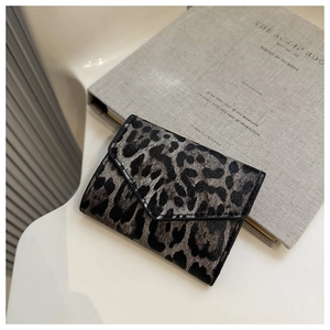 Dettaglio del mini portafoglio leopardato a bustina su sfondo di un libro decorativo