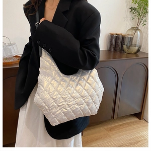 Silver quilted metallic shoulder bag with adjustable strap worn by a model in a home setting