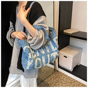 Détail d'un grand sac cabas en jean avec broderie de lettres blanches et bords effilochés