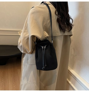 Dettaglio di una borsa a secchiello nera con coulisse indossata da una modella in interno