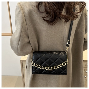 Close-up of black quilted crossbody bag with decorative gold chain and leather texture