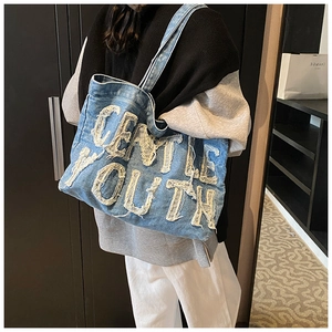 Détail d'un sac cabas en jean bleu avec écussons lettres GENTLE YOUTH effilochés