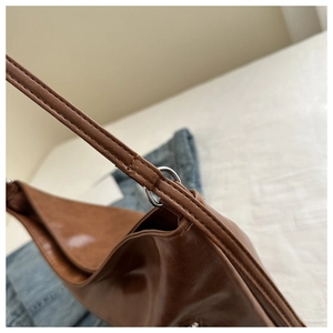 Dettaglio borsa in pelle marrone con cuciture sottili e anello a D in metallo argento