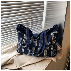 Vue détaillée d'un grand sac fourre-tout en denim avec des écussons à lettres effilochés