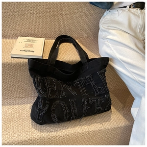 Gros plan du sac cabas en denim noir avec broderie GENTLE YOUTH effilochée sur escalier