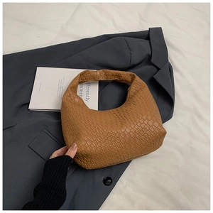 Close-up of caramel brown woven hobo bag with intricate leather texture on white linen
