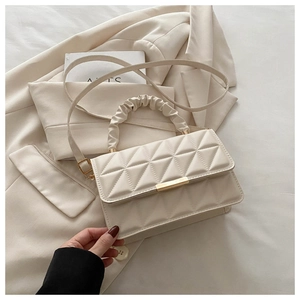 Close-up of quilted cream handbag with pleated handle and golden metal bar detail