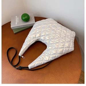 Close-up of quilted white crescent bag with glossy texture and black strap on wooden table
