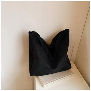 Detail view of large black suede tote bag placed on books in a minimalist setting