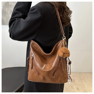 Dettaglio della borsa hobo vintage in pelle marrone con tasche zip e ciondolo a orsetto