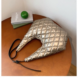 Macro shot of champagne gold quilted crescent tote bag with metallic finish on a wooden table