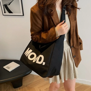 Retro black canvas tote bag with MOAD lettering shown on a model in a minimalist room