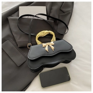 Detail of black wave-edge leather handbag with golden bow metal ornament and handle