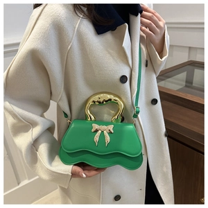 Detail of green wavy-edged crossbody bag with gold bow handle and heart ornament