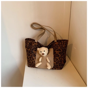 Detail view of leopard print tote bag with brown leather pocket and plush bear charm decoration