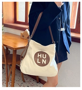 Detailed view of white canvas tote bag with brown leather straps and logo patch