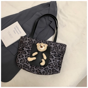 Detail of grey leopard print tote bag with black leather pocket and plush bear decoration