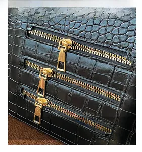Macro view of black crocodile pattern leather with three decorative gold zippers
