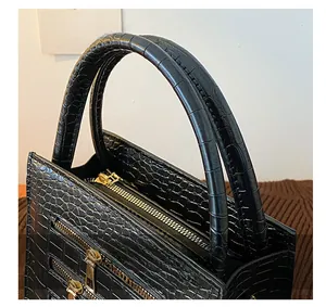 Close-up of black crocodile pattern handbag showing dual handles and gold zipper details