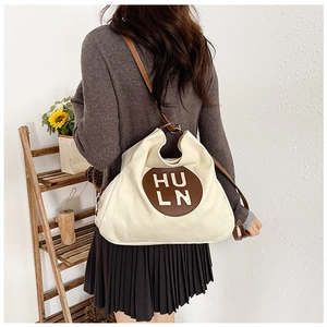 Close-up of a large beige tote bag with a brown leather logo and adjustable straps