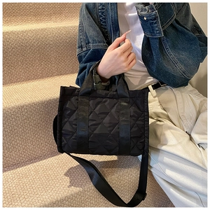 Detail view of a black quilted handbag with diamond patterns on a casual model outfit