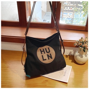 Close-up of black canvas tote bag with circular embossed HULN letter patch and brown strap