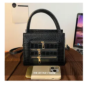 Close-up of black crocodile embossed handbag with three decorative metal zippers