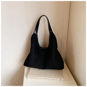 Detail van minimalistische zwarte hobo-tas in mat suède textuur op een kunstboek