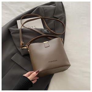 Dettaglio della borsa a secchiello in ecopelle marrone con scritta FASHION su blazer grigio