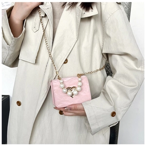 Detail of pink mini crossbody bag with pearl heart buckle on beige trench coat
