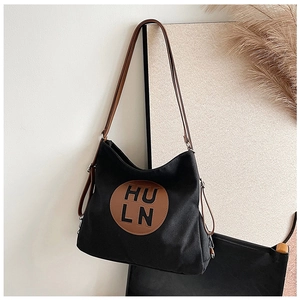 Detail of black canvas tote bag with brown leather logo patch and thin leather shoulder straps