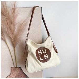 Detail of off-white canvas tote bag featuring brown leather logo patch and thin straps