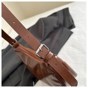 Macro detail of brown glossy PU shoulder bag showing textured material and silver metal buckle