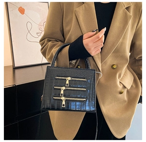 Detail of black crocodile texture bag with gold zippers and detachable shoulder strap