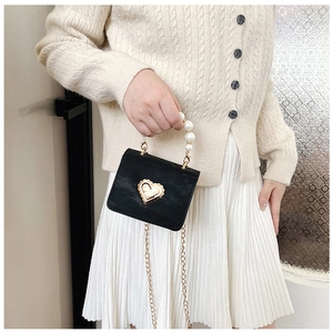 Detail of a mini black crossbody bag featuring a gold heart clasp and pearl handle strap