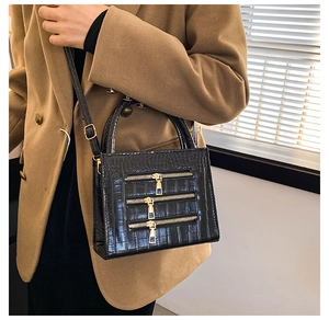 Detail of black crocodile texture bag with decorative gold zippers on a stylish suit