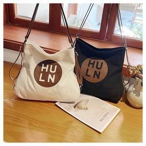 Detail of canvas tote bags in beige and black with embossed circular leather logo