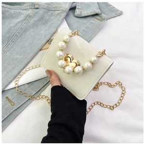 Close-up of white crossbody bag featuring pearl handle and golden heart-shaped lock